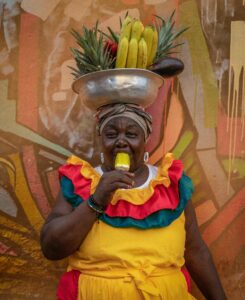 Vibrant street vendor in traditional attire enjoying fruit in Cartagena, Colombia.