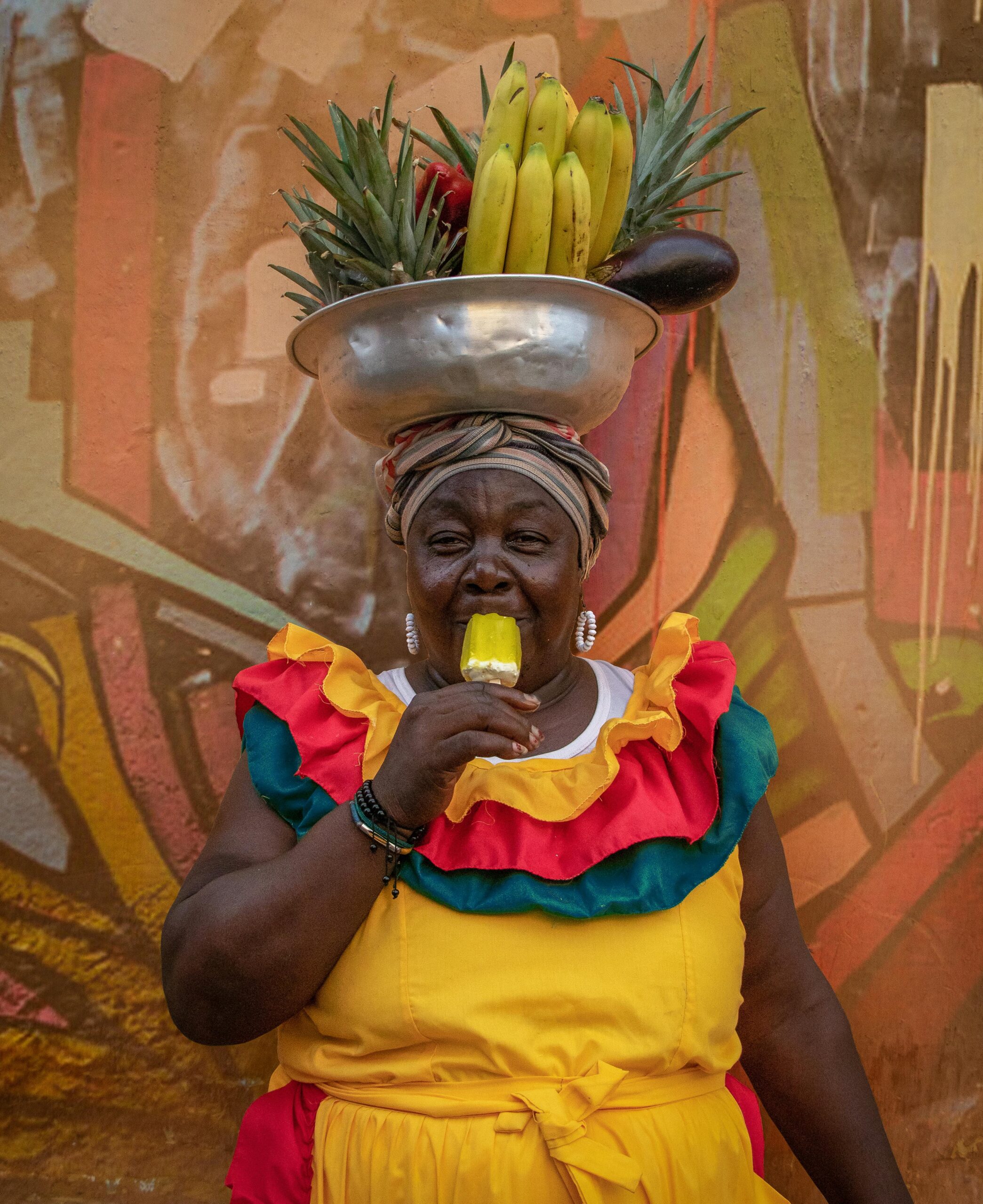 Vibrant street vendor in traditional attire enjoying fruit in Cartagena, Colombia.